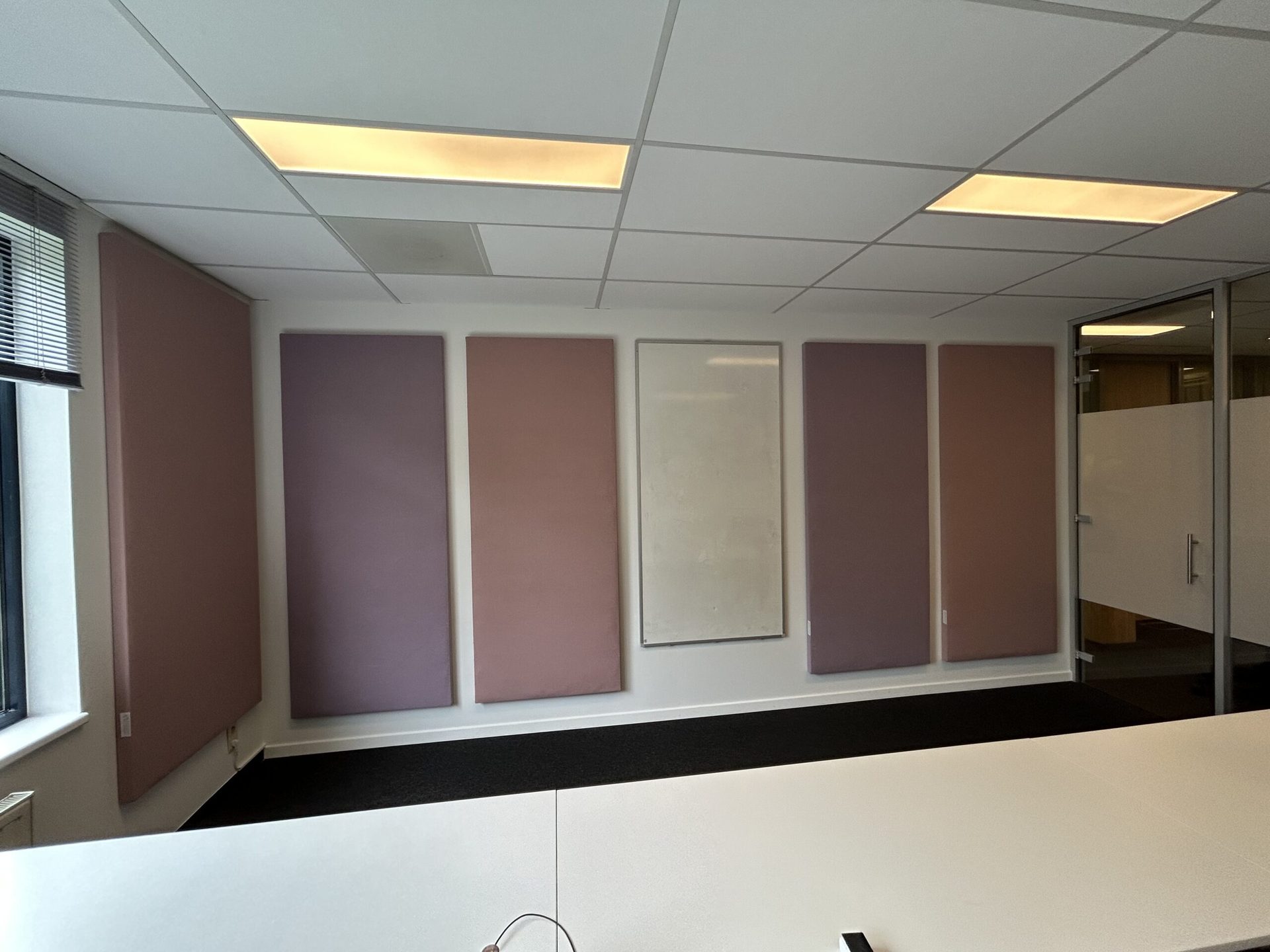 Akoestische wandpanelen in zachtroze tinten aan de wand van een kantoor